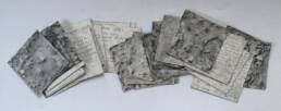 A row of small squares of paper spread out in a horizontal line, showing a mix of pencil ground rubbings and the written text on the back.
