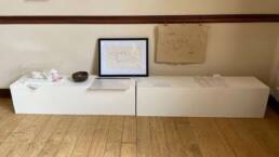 two plinths on the floor with a line of artworks on the top