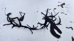 black ink branch forms cut out with black ink spots on paper behind it